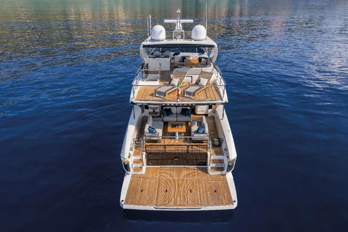 Luxury motor yacht viewed from above, featuring sun loungers, seating area, and Italian flag on the deck, surrounded by water.